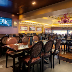 Tom restaurang med mörka träbord, vadderade stolar, inramade minnessaker, en monterad TV och en ljuskrona. "ÄLSKA ALLA, TJÄNA ALLA."