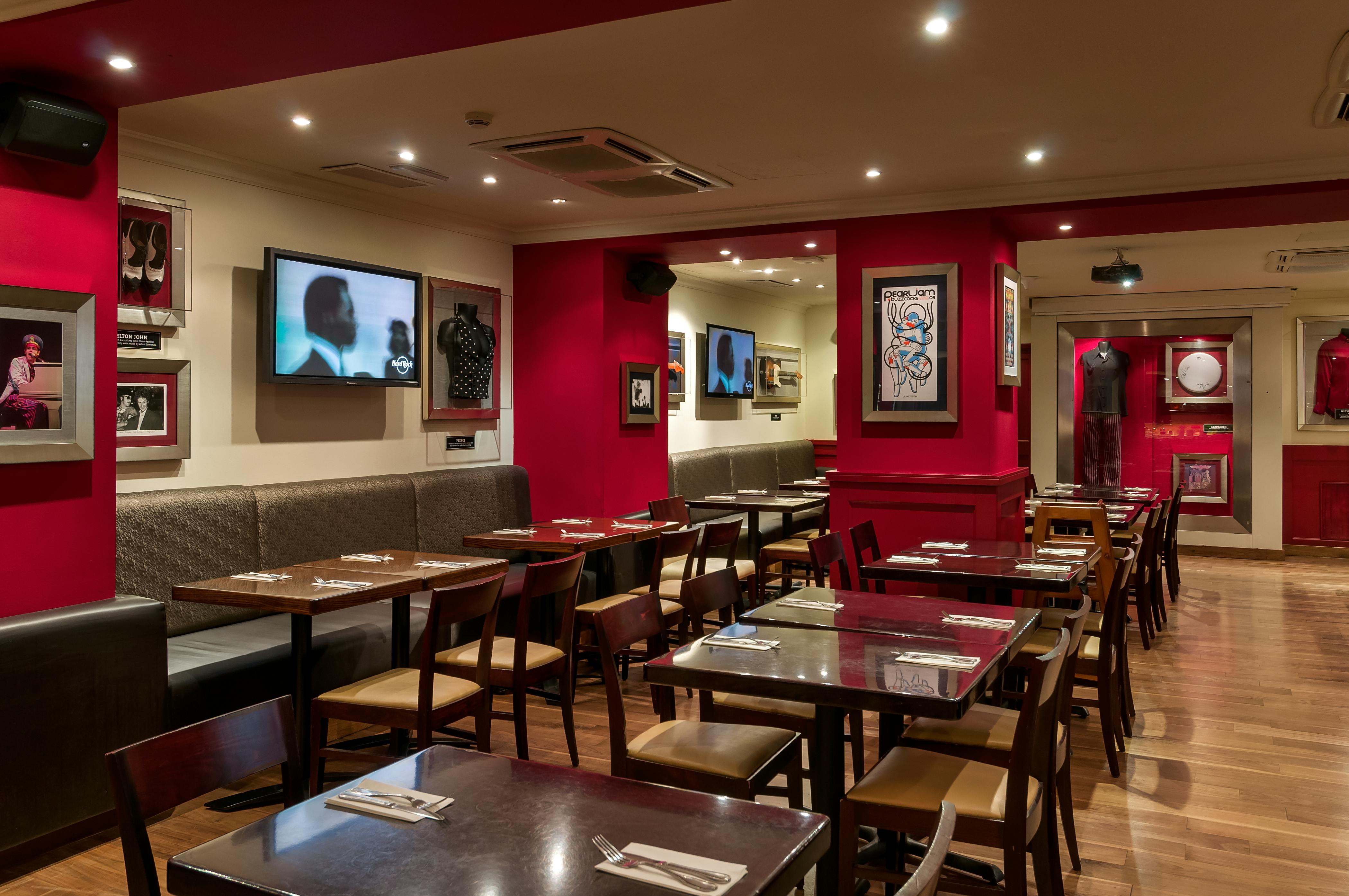 Un intérieur de restaurant avec des murs rouges, des œuvres d'art encadrées, des écrans de télévision, des tables en bois et des chaises soigneusement disposées avec des couverts.