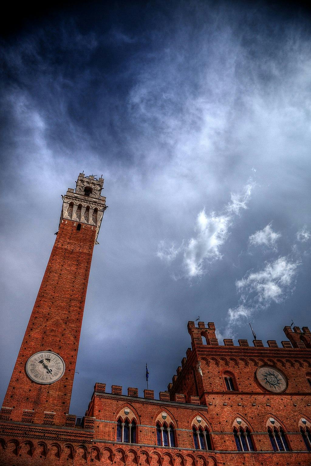 A tall brick tower with a clock, part of a historic building under a cloudy sky.