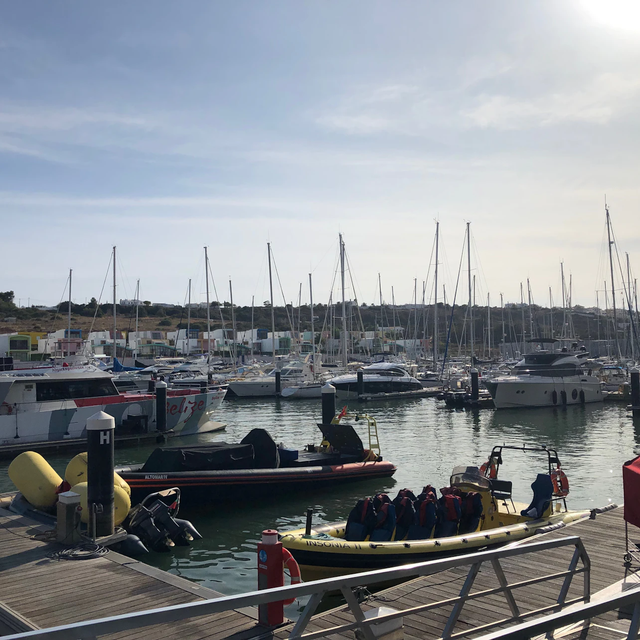 A marina with various docked boats, including sailboats and motorboats, under a partly cloudy sky.
