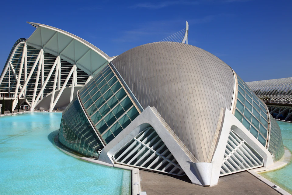 Futuristic building with a dome shape, large glass panels, and surrounding water under a clear blue sky.