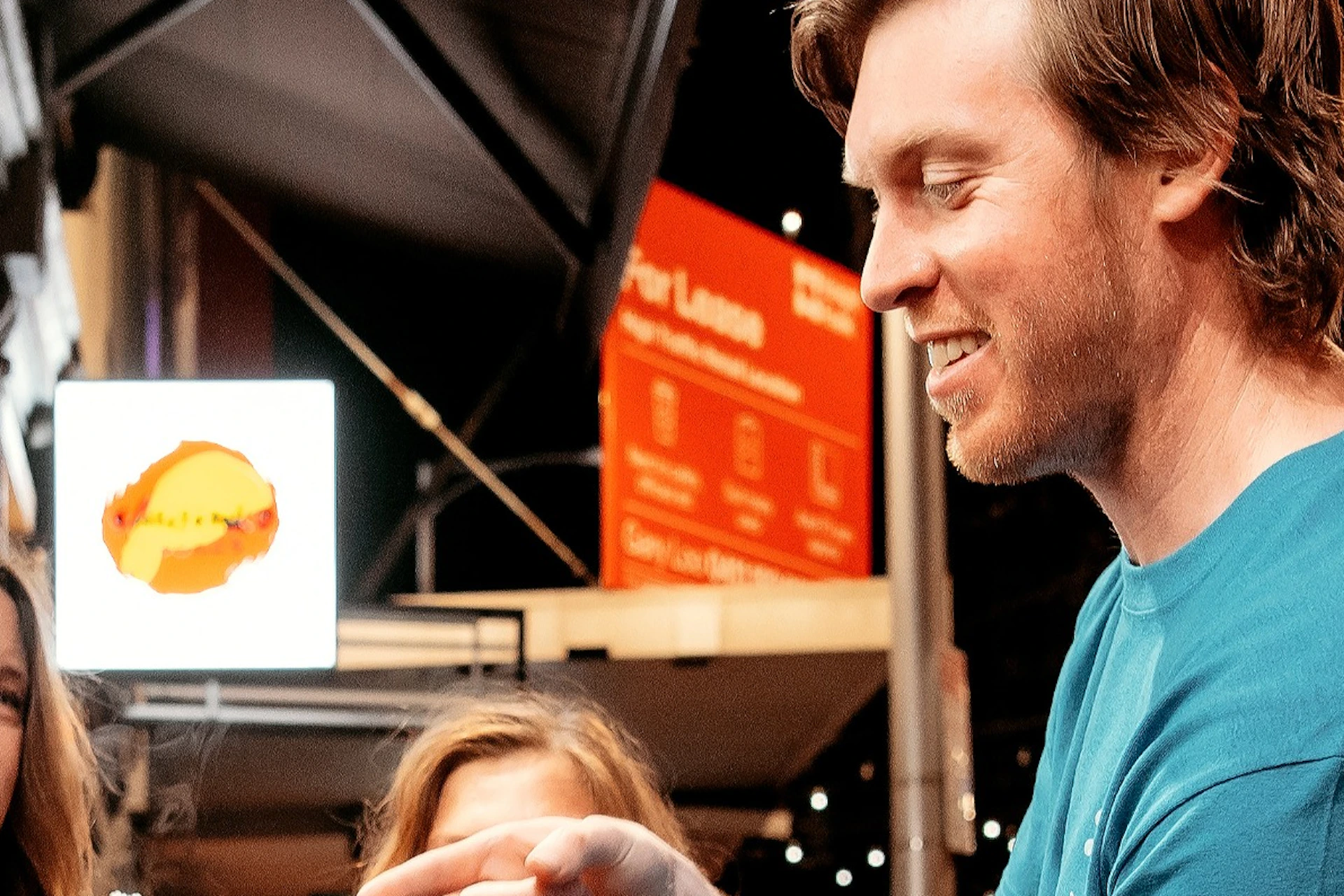 A group of five people standing outside a Chinese restaurant at night, sharing food and talking under bright signage.