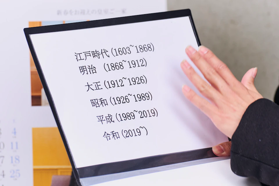 A person holding a document listing Japanese historical periods with their respective dates.
