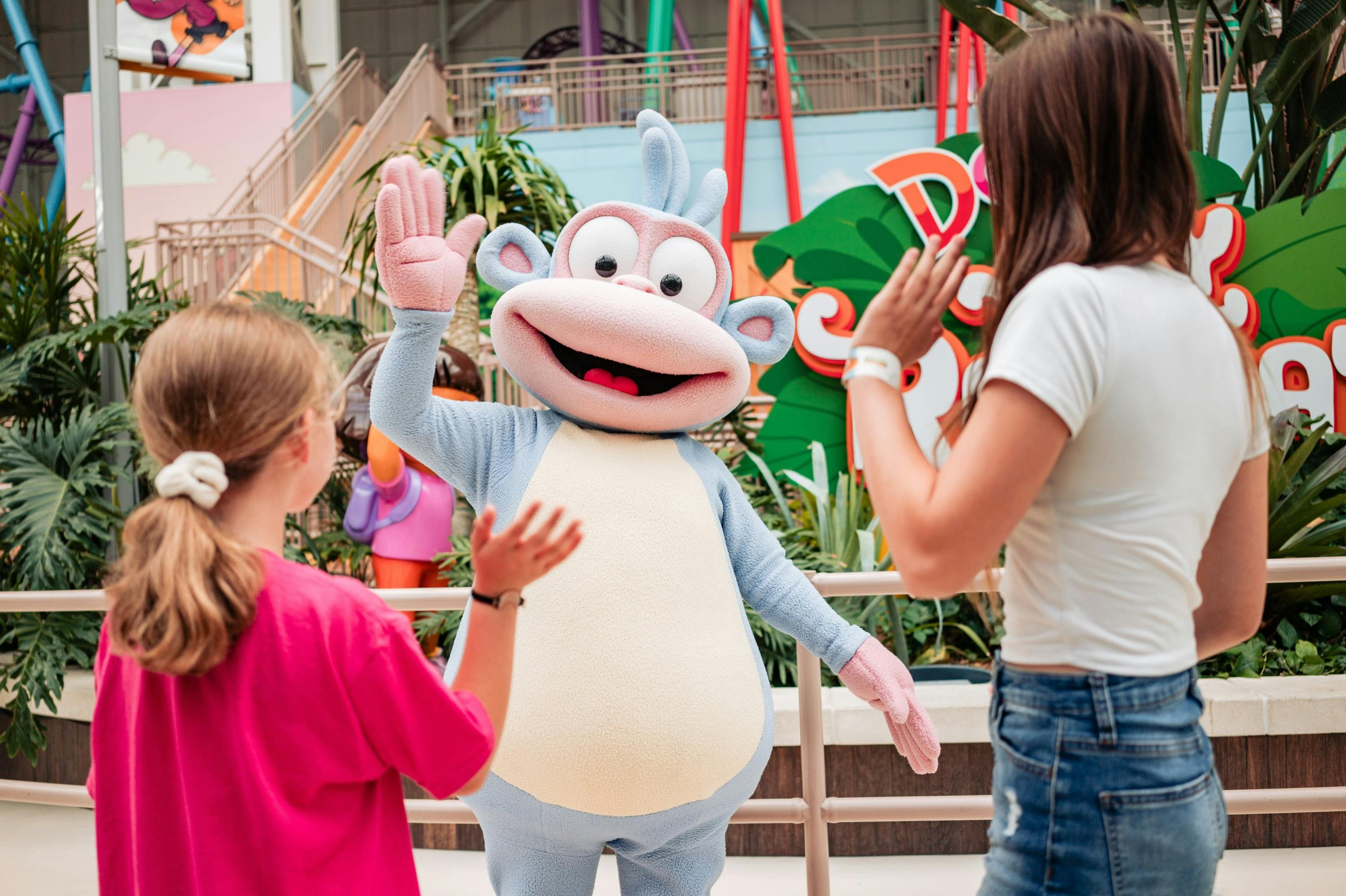 A person in a cartoon monkey costume high-fiving two children in an indoor amusement park setting.