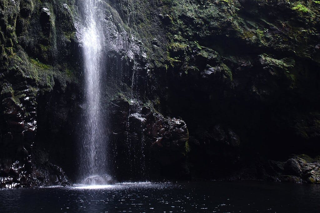 Водопад каскадом каскадирует по покрытой мхом скале в темный, спокойный бассейн внизу.