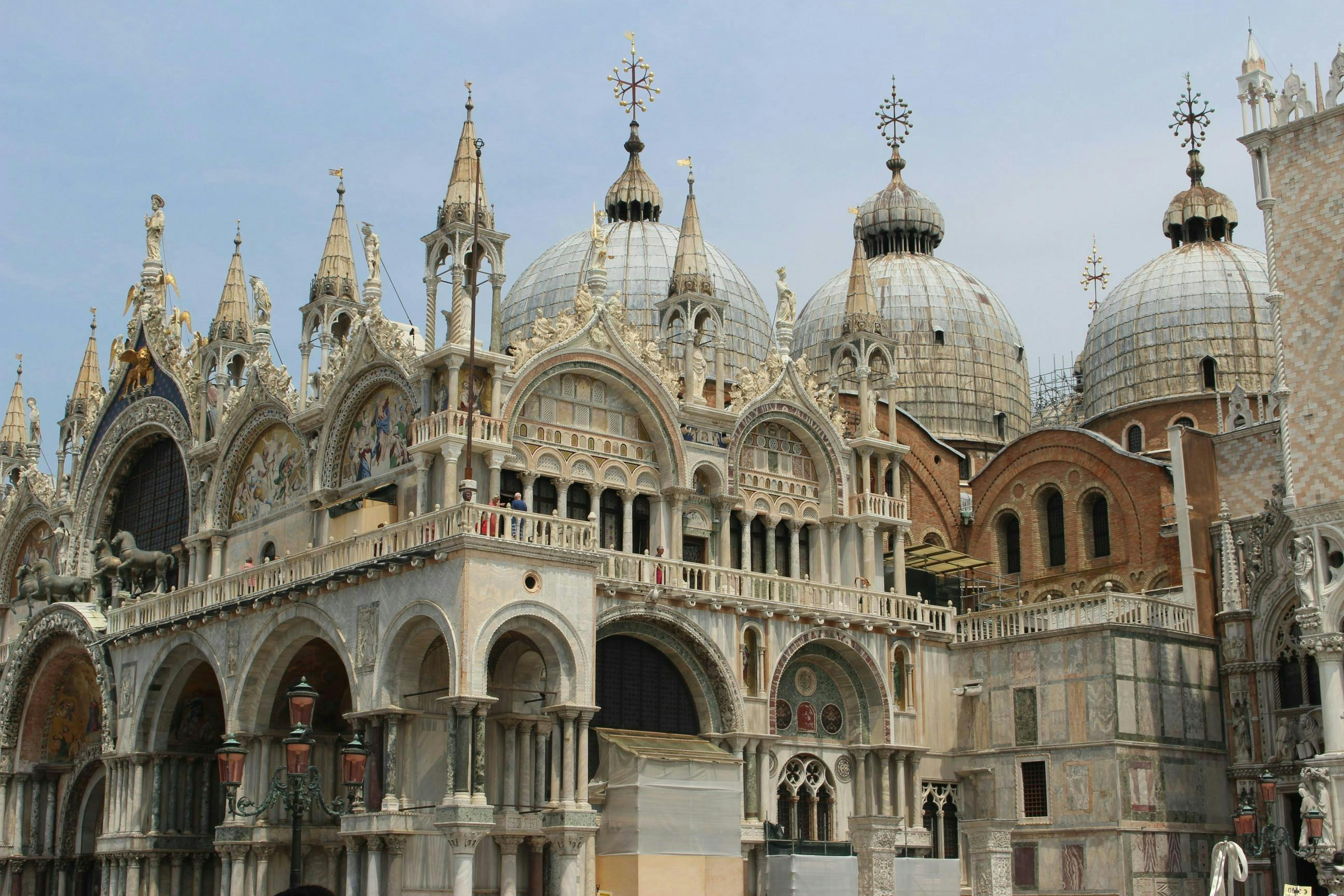 Ornate cathedral with arched windows, intricate facades, and multiple domes under a clear sky.