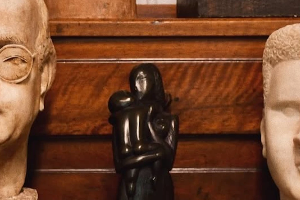 A collection of sculptures on a wooden shelf, including two busts and a central abstract figurative statue.
