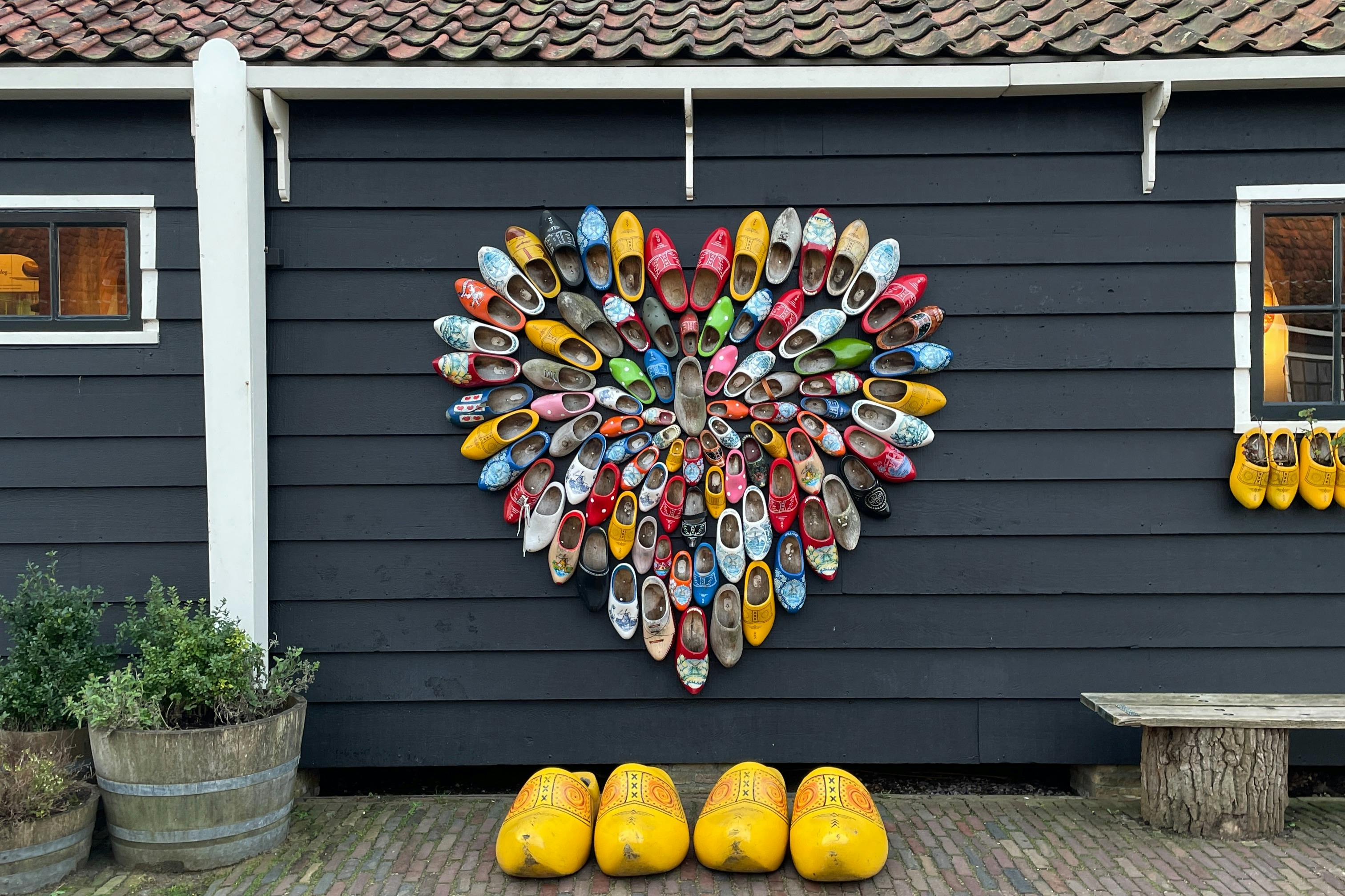 A heart-shaped arrangement of colorful wooden clogs mounted on a dark wall, with large yellow clogs on the ground below.