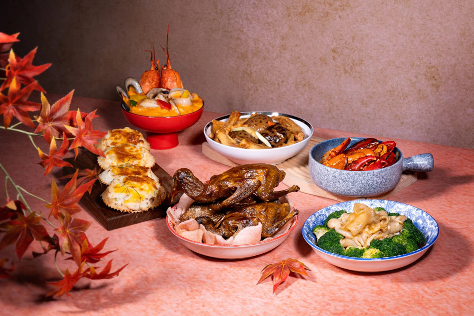 A variety of cooked dishes displayed on a table, including seafood, roasted meat, and vegetables, with autumn leaves as decoration.