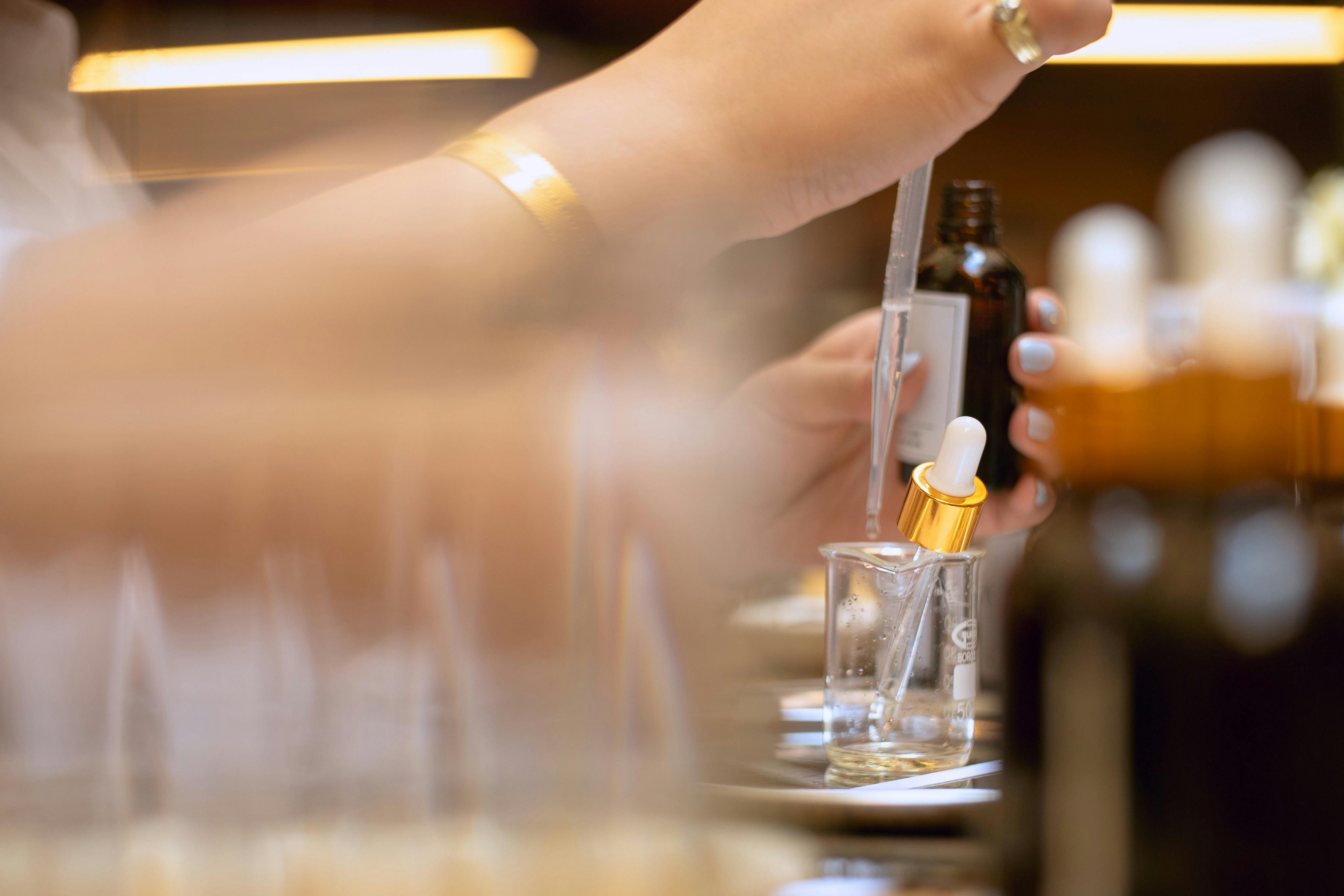 A person carefully mixing perfume ingredients with a dropper and beaker during a hands-on workshop.
