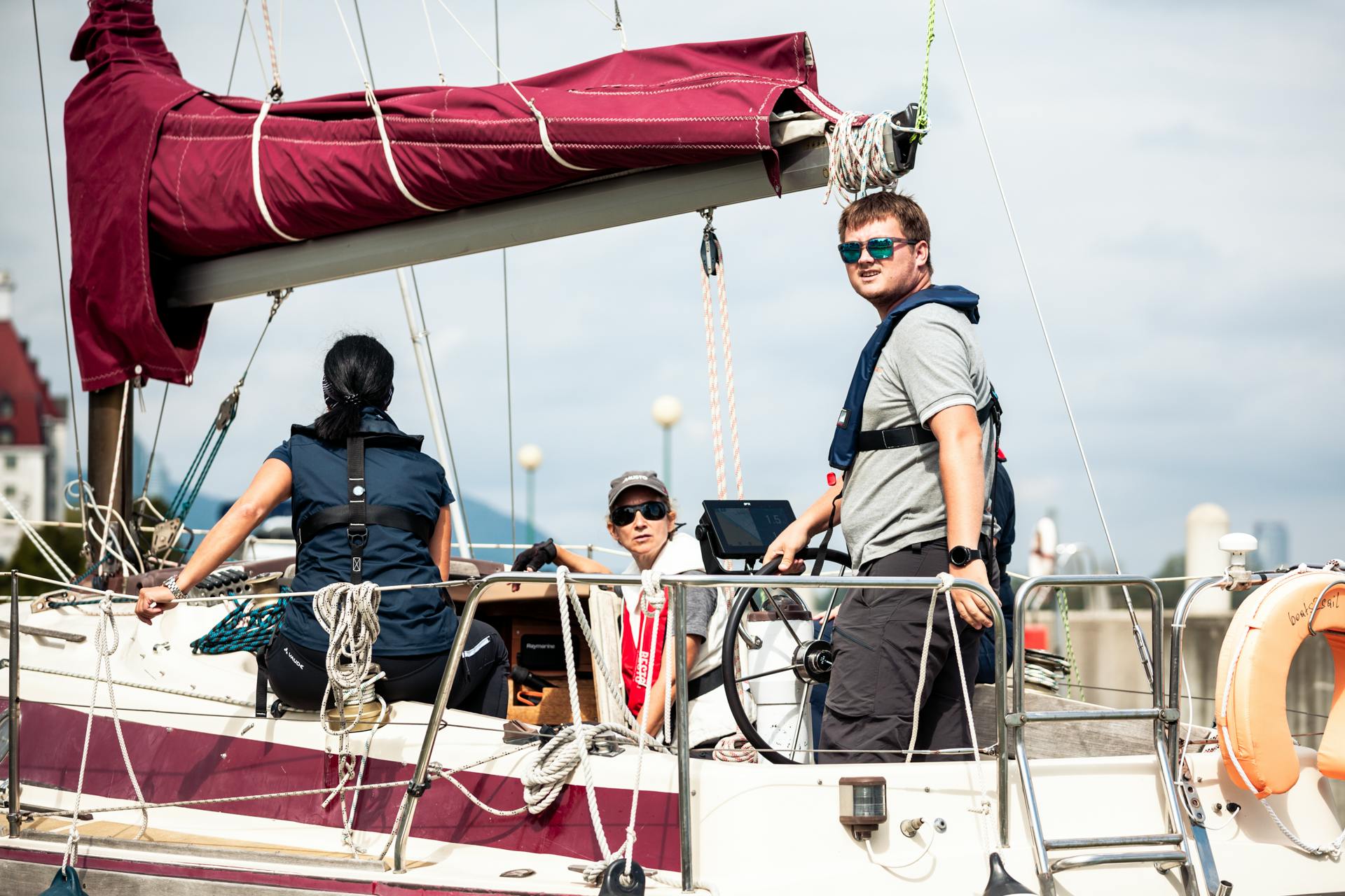 帆船に乗っている3人、1人のステアリング。 帆はマルーンカバーで包まれ、ロープはデッキできれいに巻かれています。