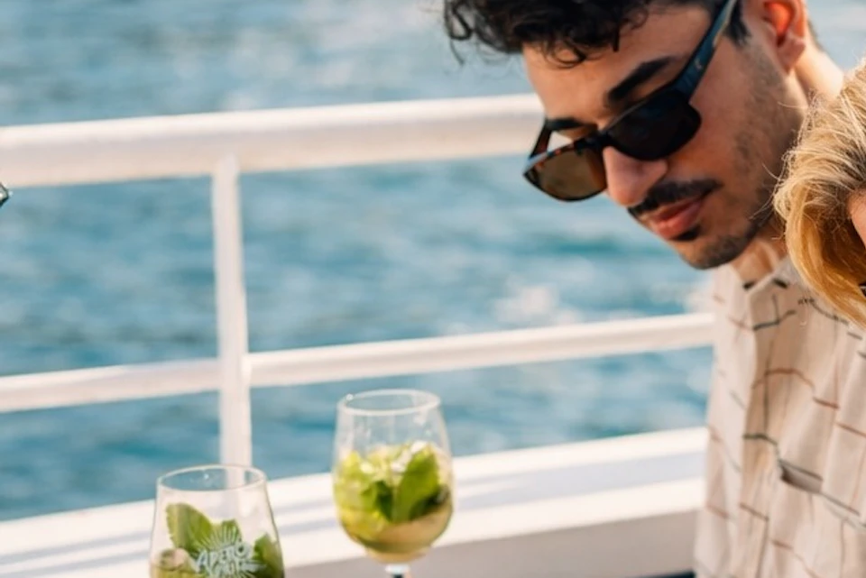 Three people seated at a table on a boat, looking at a map, with glasses of green beverages on the table.