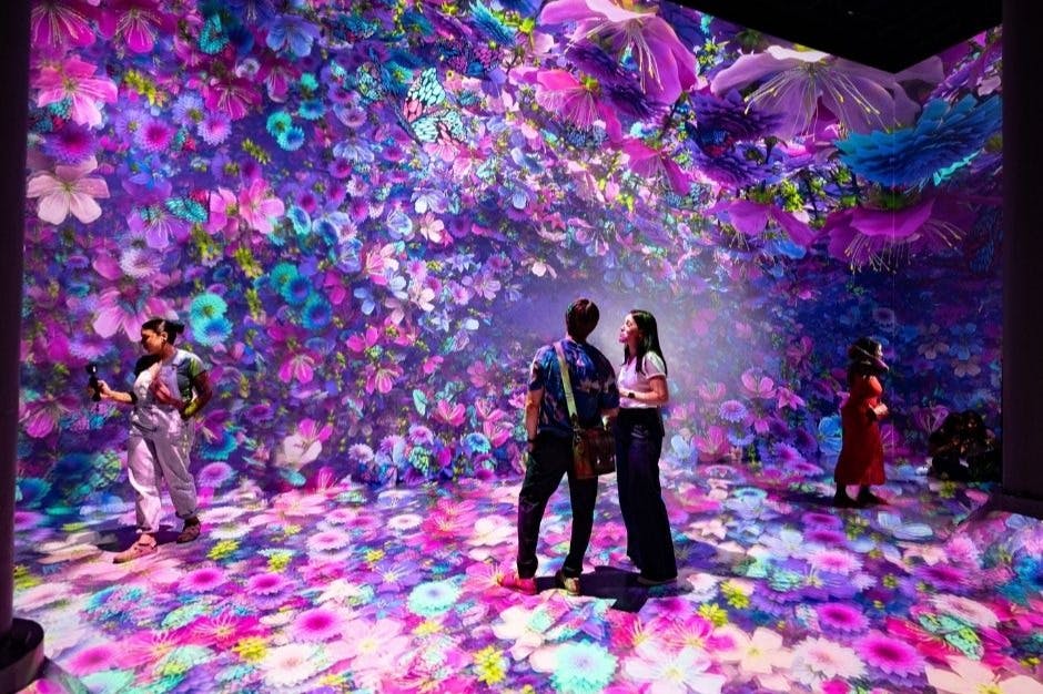 カラフルな花の鮮やかなデジタル投影に囲まれた没入型アート展に2人が立っています。