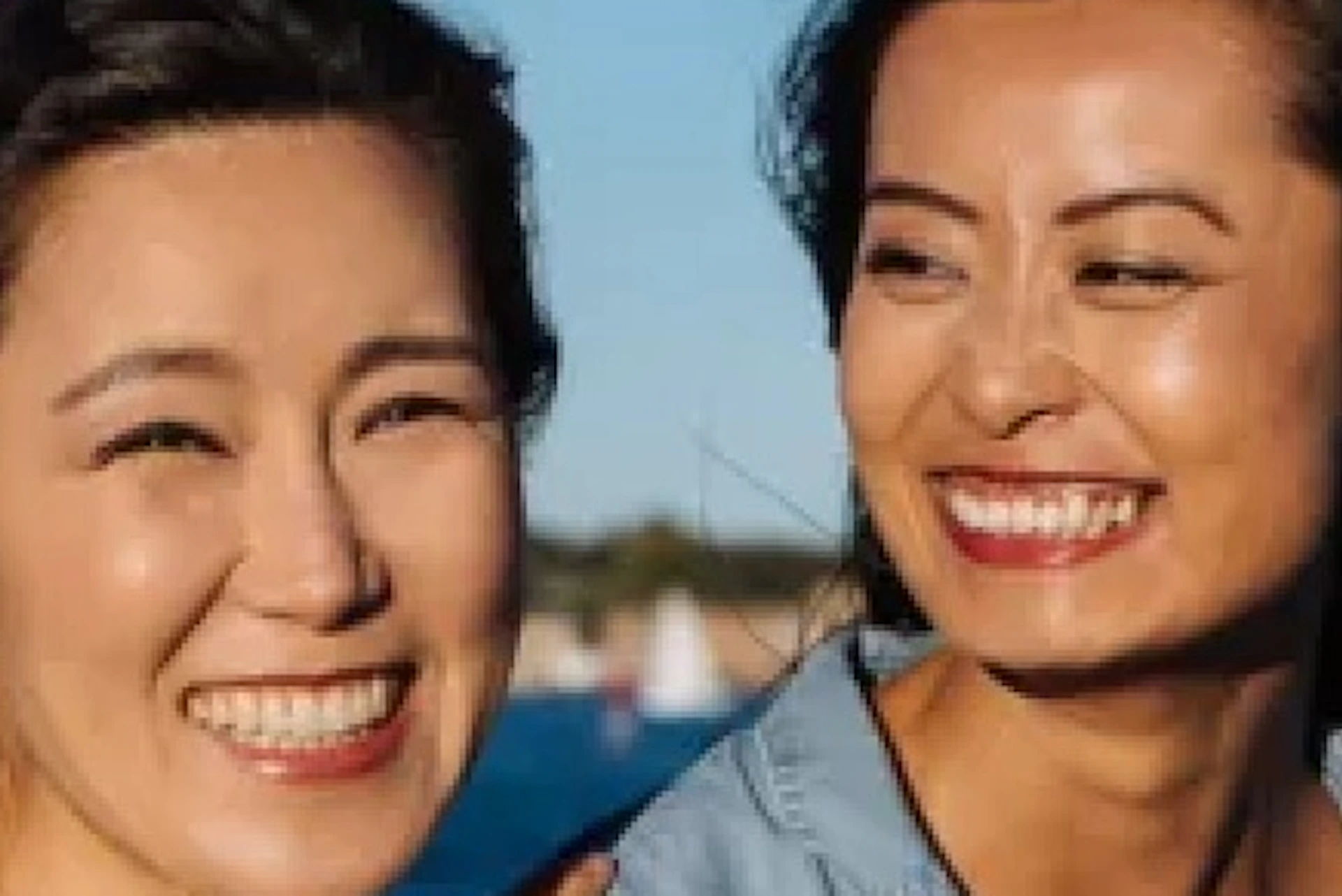 Two women smiling on a boat with water and the Sydney Opera House in the background under a clear blue sky.