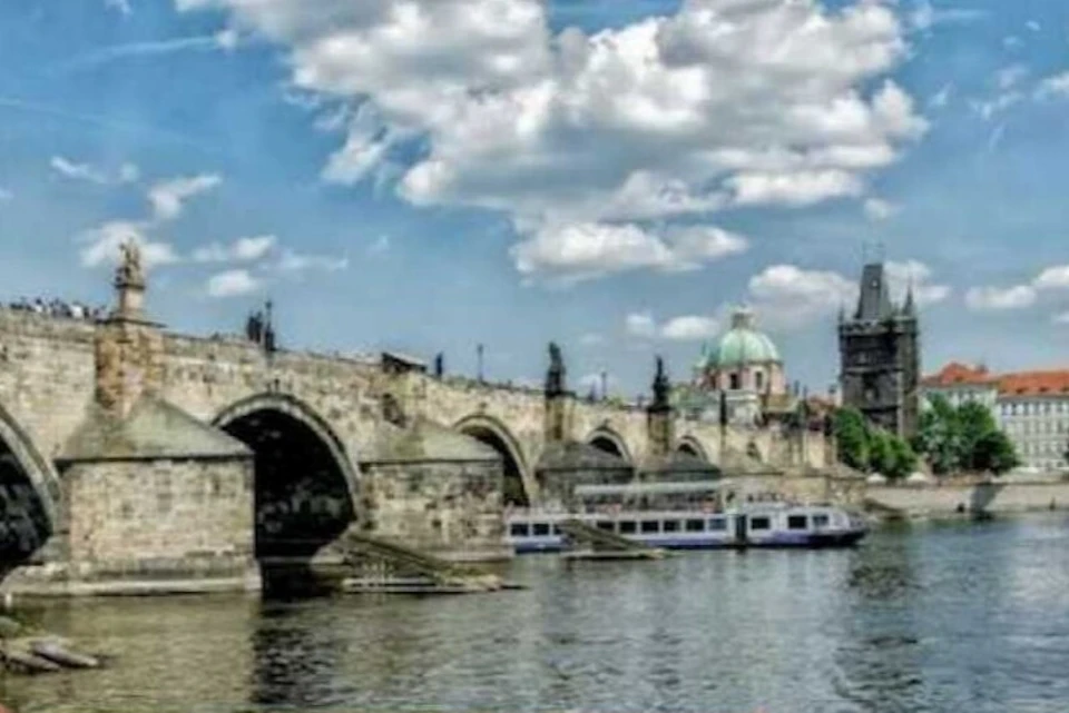 A stone bridge with arches spans a river; boats float underneath, and a domed building is visible in the background.