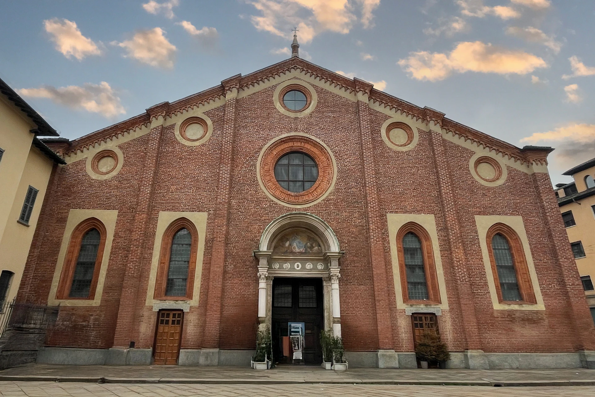 A red brick church with arched windows and a central circular window, under a partly cloudy sky.