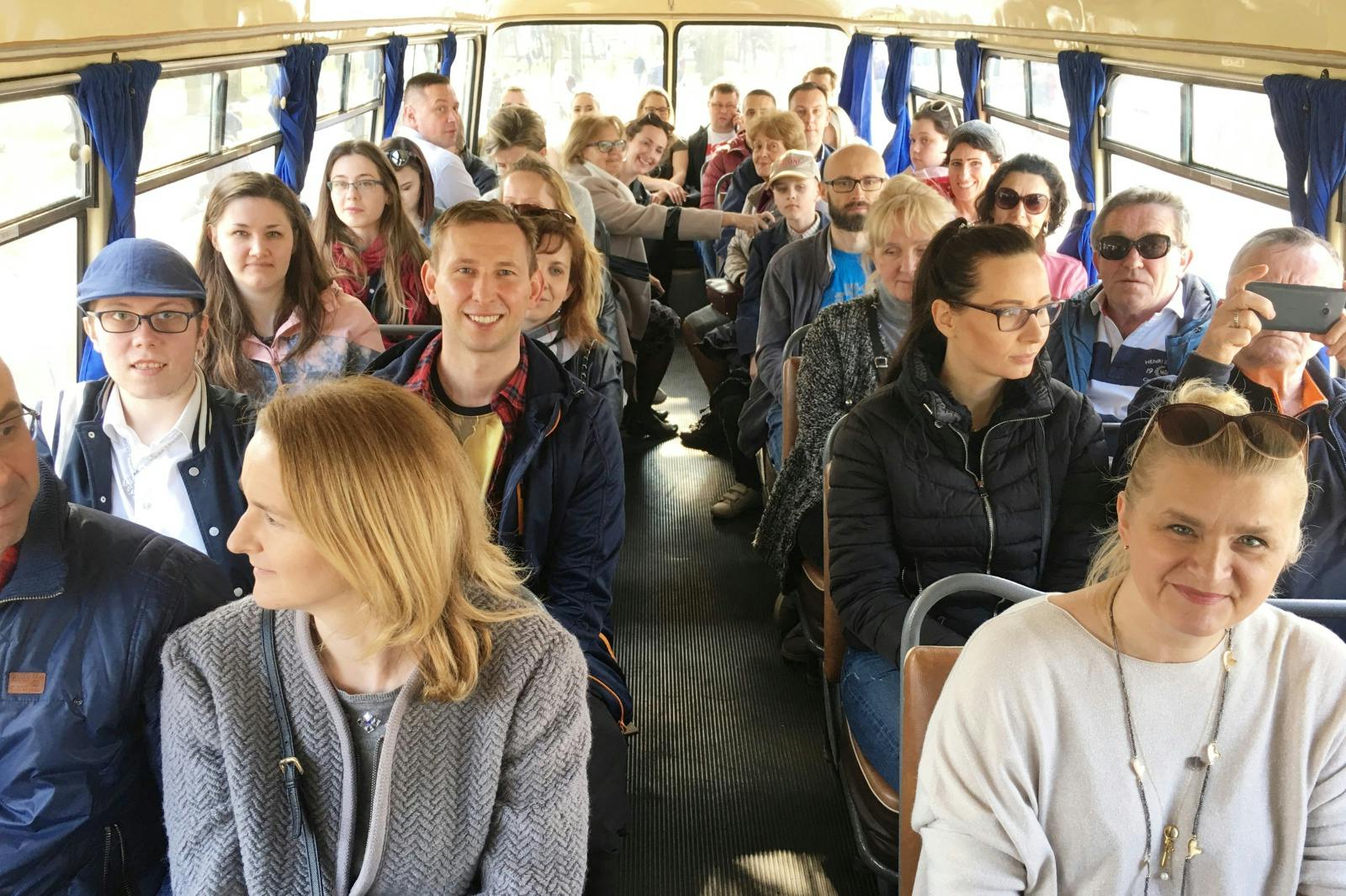 座って立っていて、前を向いていて、さまざまな方向を見ているさまざまな年齢の乗客で混雑したバス。