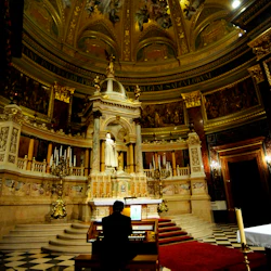 En person spelar en orgel i en stor katedral med utsmyckade dekorationer, ett stort altare och en rikt målad kupol.