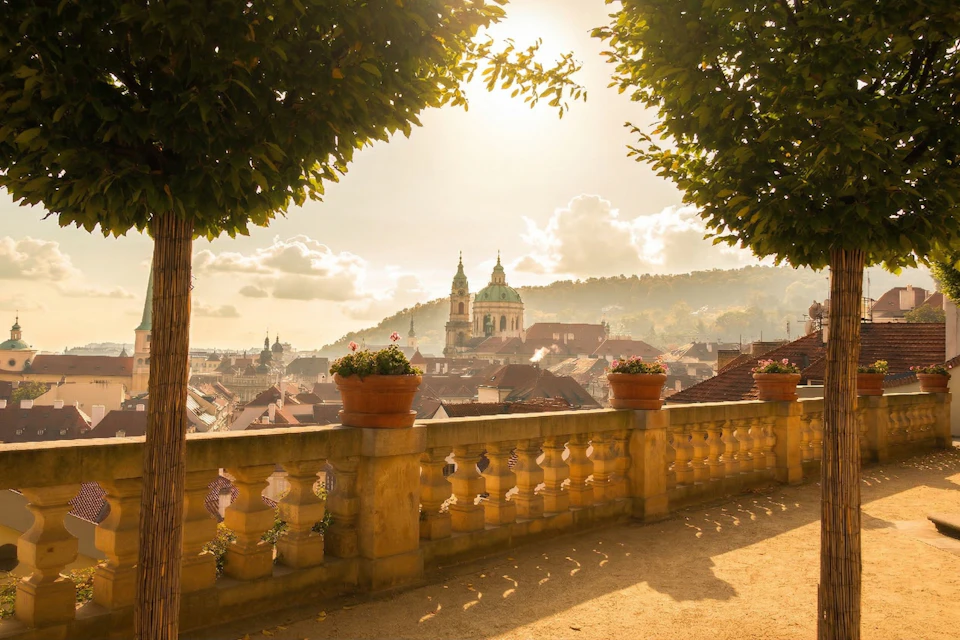 A scenic view of a city at sunset, with a balustrade adorned with potted plants, and a church visible in the distance.