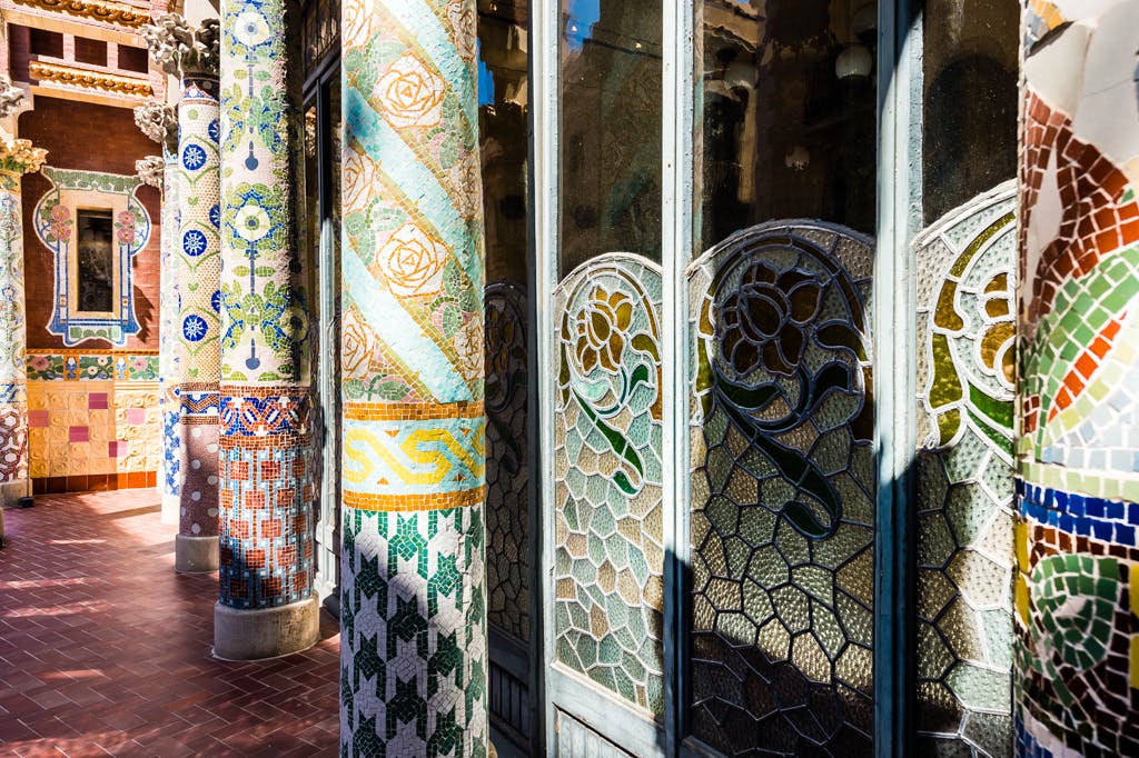 Dekorative Kachelsäulen und Buntglasfenster mit floralen Motiven, verschlungenen Mustern und leuchtenden Farben.