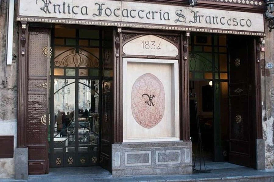 Entrance of "Antica Focacceria S. Francesco," with ornate decorations, glass door, and "1834" inscribed above a large emblem.