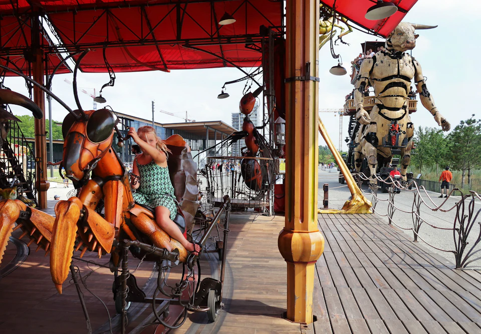 Child riding a mechanical insect under a red canopy. Large animated structure of a humanoid figure in the background.