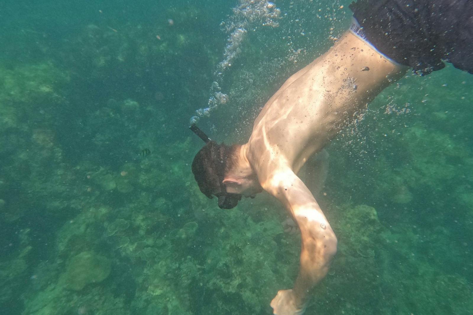 Osoba šnorchlující v čisté vodě, s maskou na šnorchl. Sluneční světlo filtruje a osvětluje podvodní scénu.