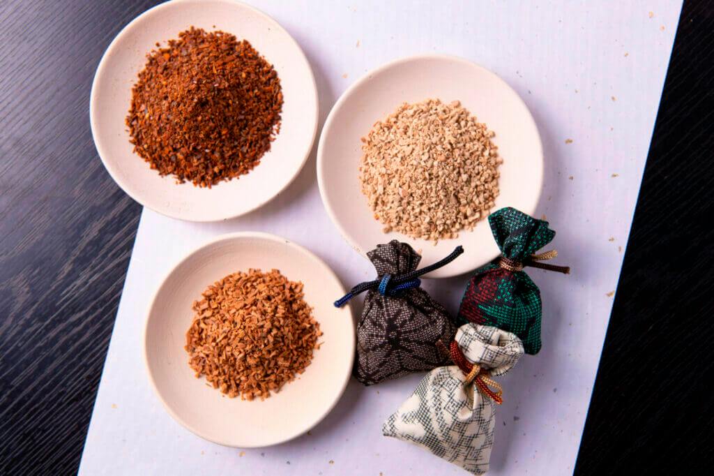 Three small plates with different ground spices and four small fabric bags tied with strings on a white surface.