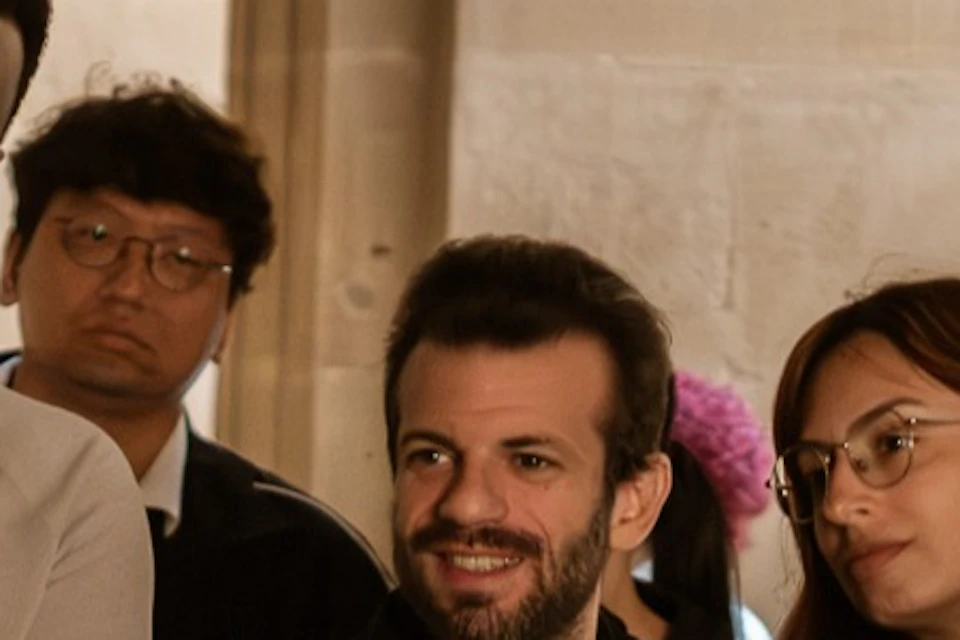A group of people gathered indoors, one holding a book and showing it to others who are smiling and engaged.