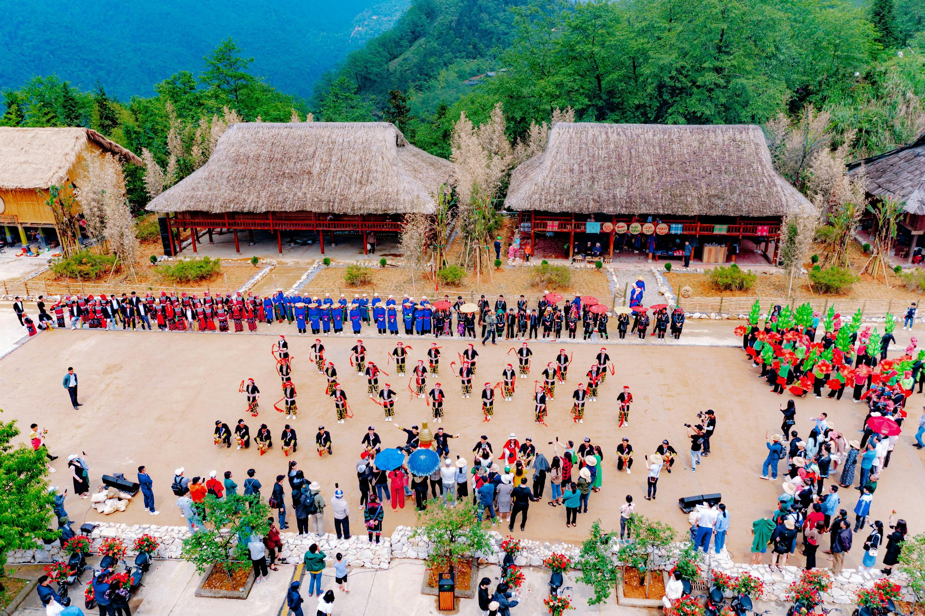 A traditional dance performance in a village setting with thatched-roof buildings, trees, and mountains in the background.