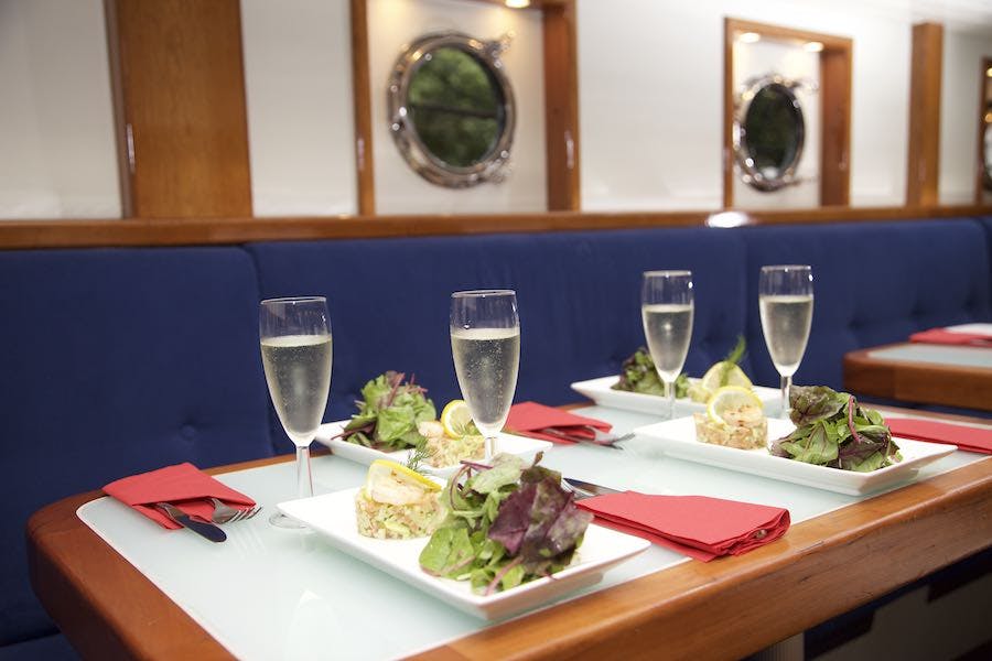 餐桌上摆放着沙拉和柠檬盘子、香槟杯、红色餐巾和用餐区蓝色软垫长凳。