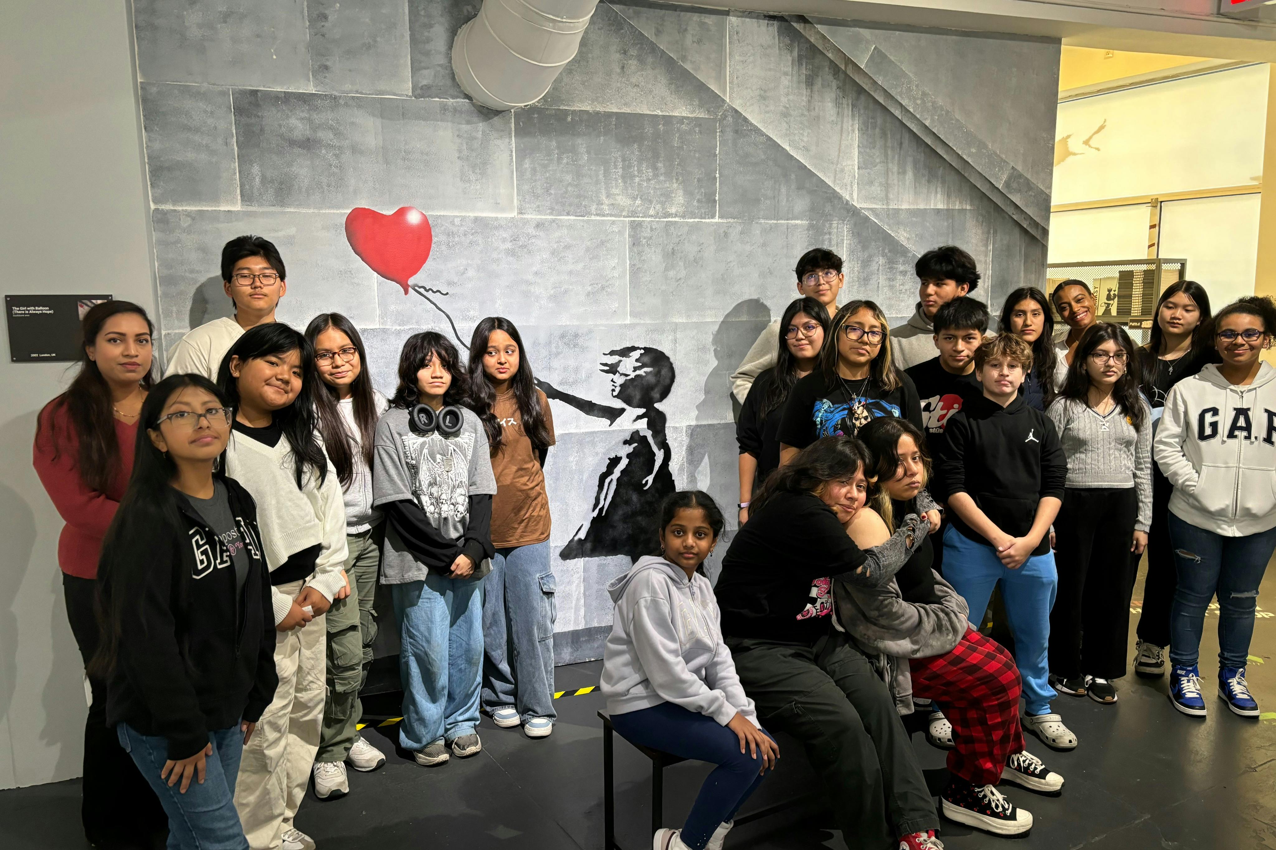 A group of people pose in front of a mural depicting a child letting go of a red balloon.