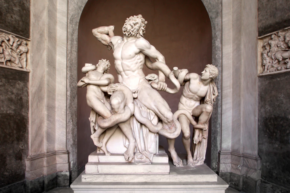 A marble statue of three male figures struggling with a large serpent, set in an arched niche.