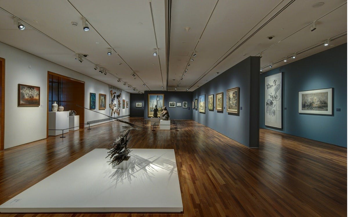 An art gallery with various framed paintings on the walls and a sculpture on a white pedestal in the center.