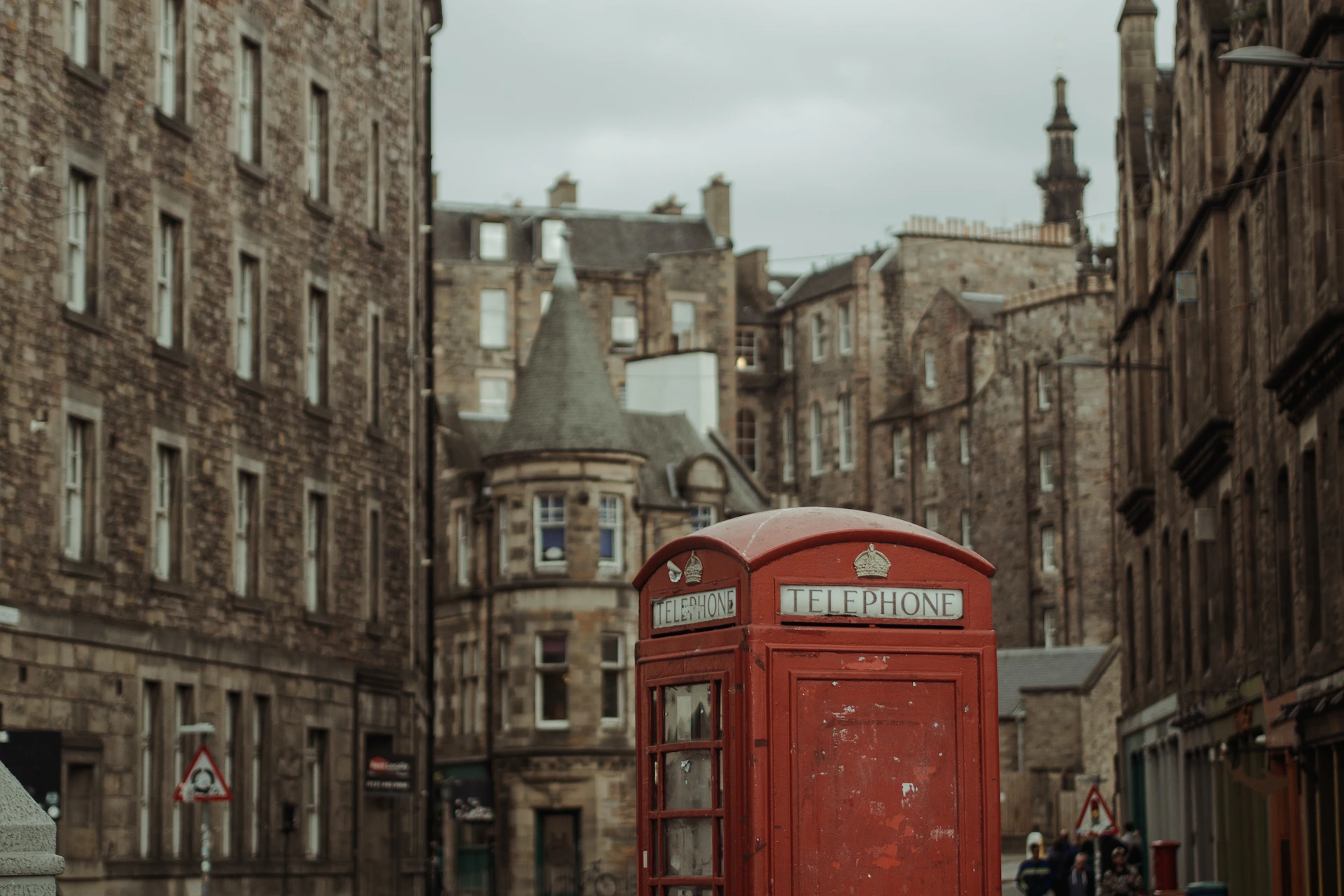 Red British phone booth in front of historic stone buildings under a cloudy sky.