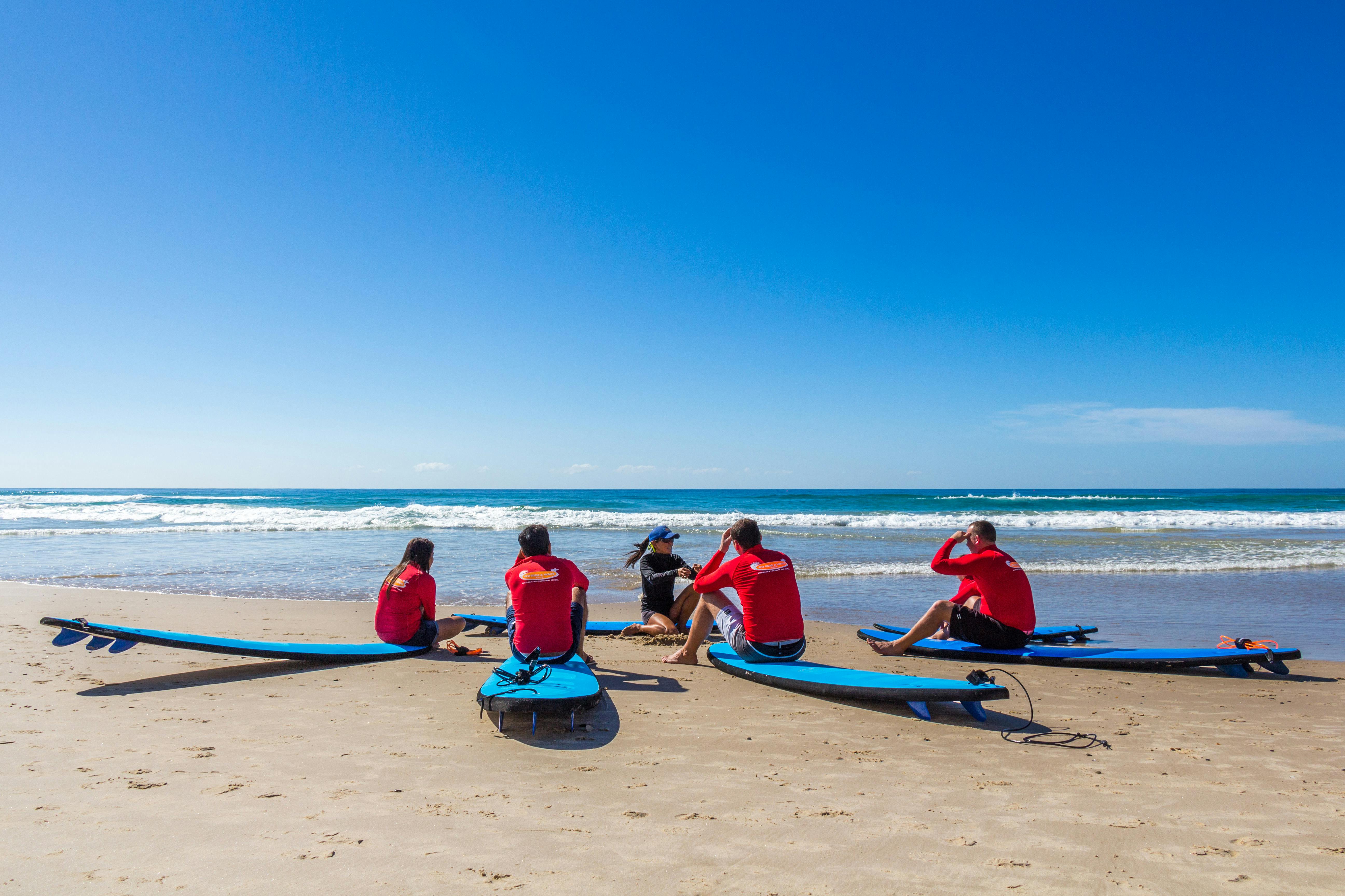 빨간 셔츠를 입은 5명이 서핑보드가 있는 해변에 앉아 맑고 푸른 하늘 아래 바다를 마주하고 있습니다.