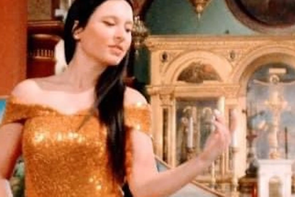 A woman in a sparkling gold dress sings between a pianist and a guitarist in an ornately decorated church.