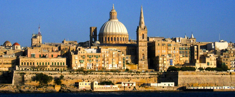 Historic cityscape featuring a large domed cathedral and a tall spire amidst numerous old buildings under a clear blue sky.