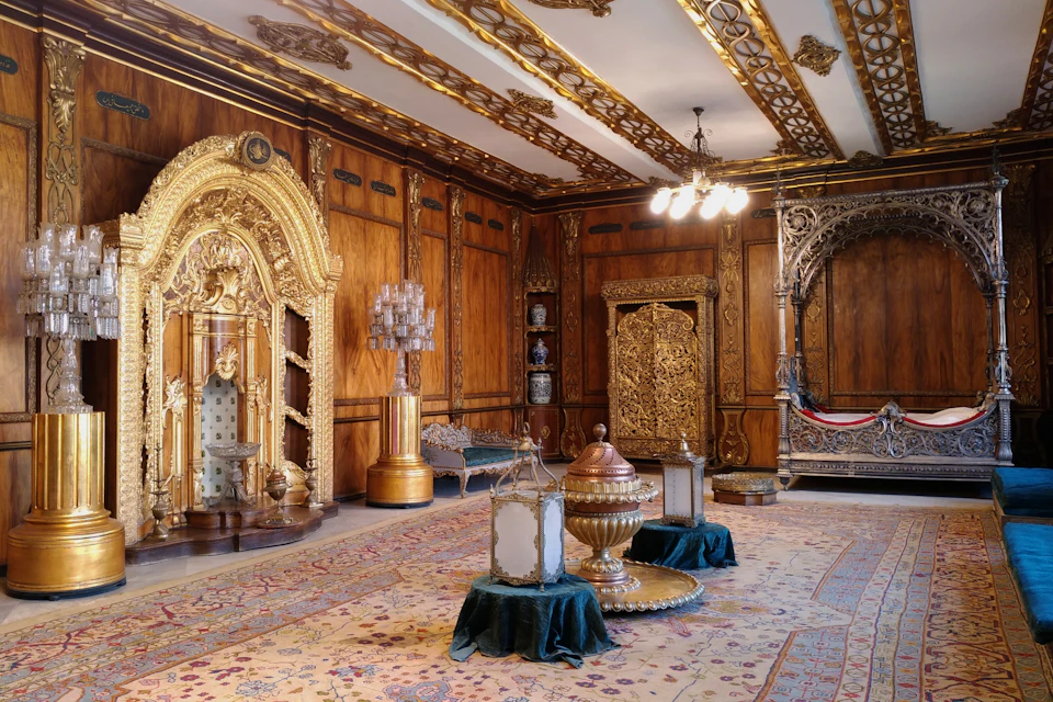 Ornate room with intricate gold decorations, chandeliers, and luxurious furniture on an elaborate carpet.