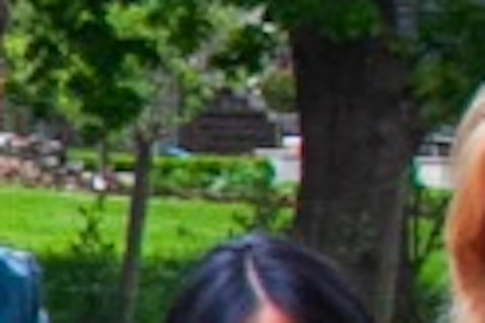 Three people pose smiling near a sign reading "Menzies Creek" in a green outdoor area with plants and buildings visible.