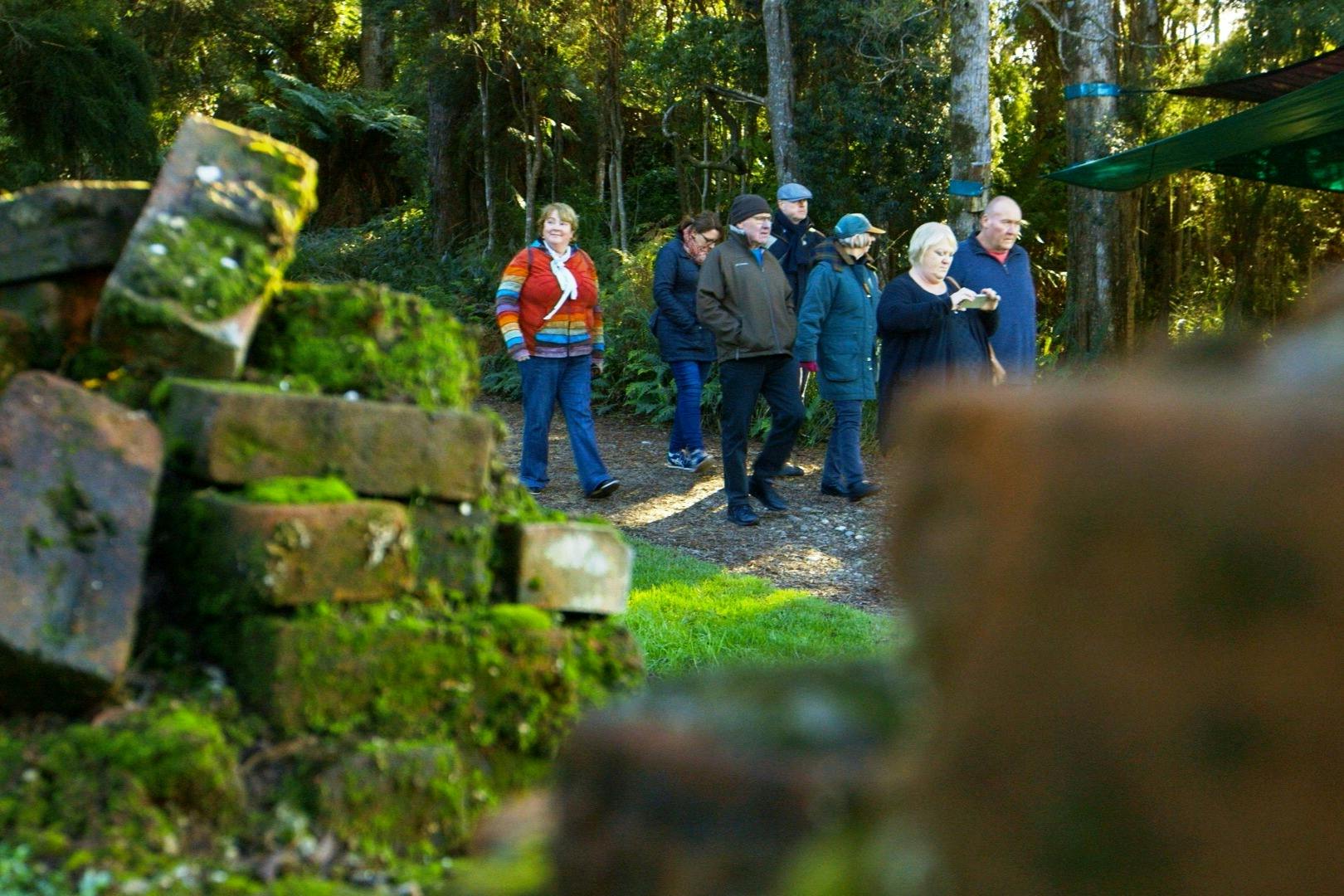 A group of people walking along a pathway in a forested area, with trees and greenery in the background.