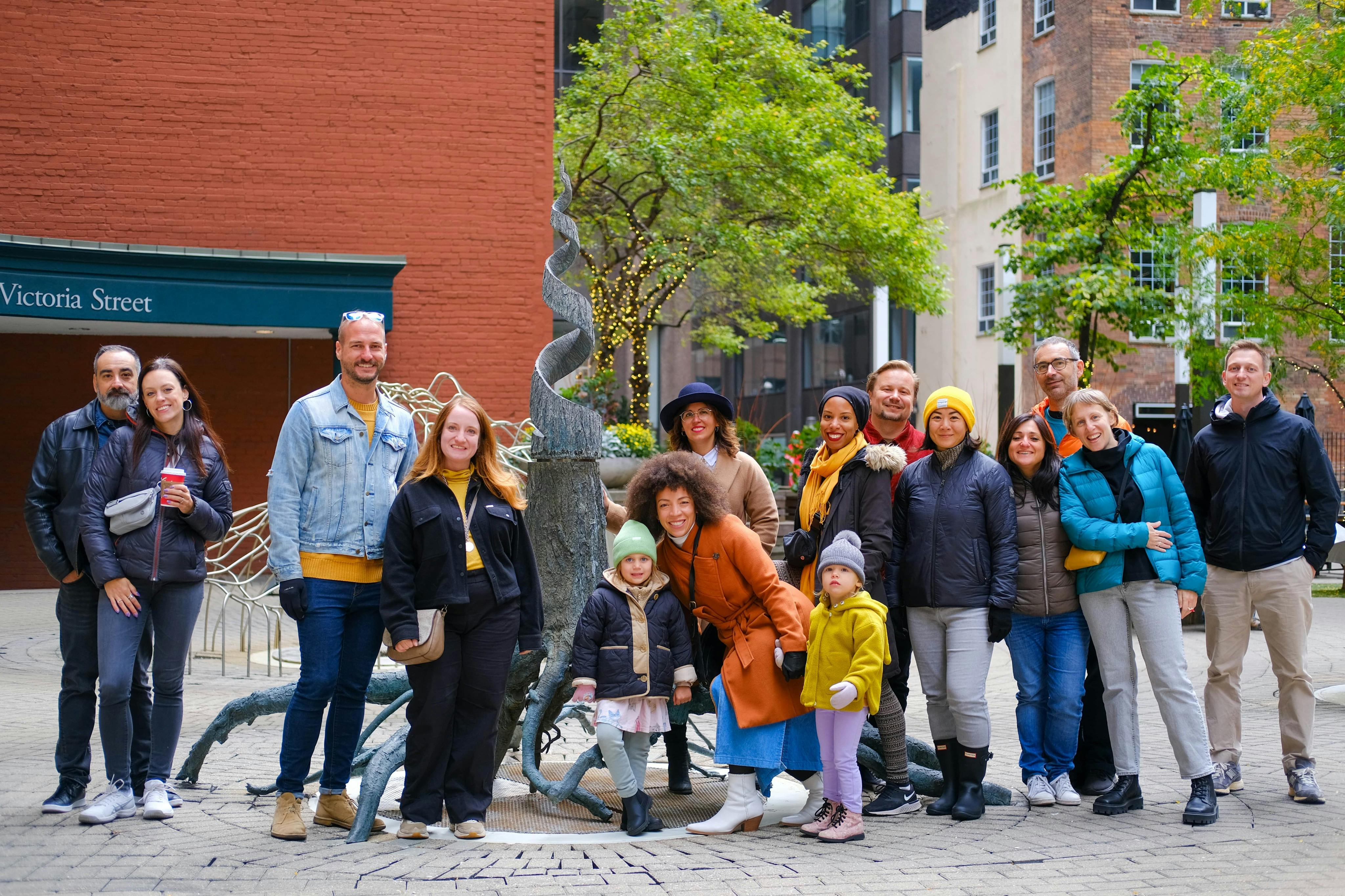 一群人在一座雕塑前面户外摆姿势，背景中有一座砖砌建筑和树木。