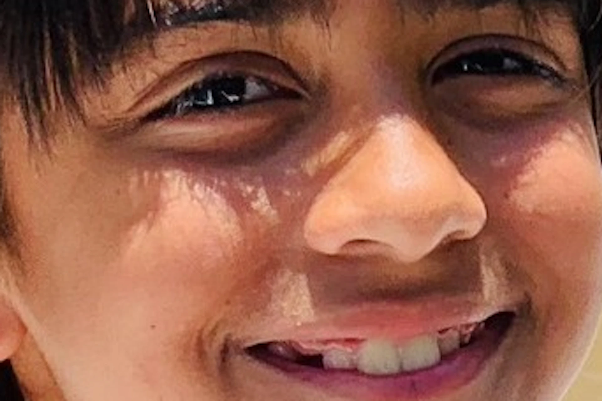 Smiling boy on a boat navigating a river surrounded by lush greenery under a bright blue sky.