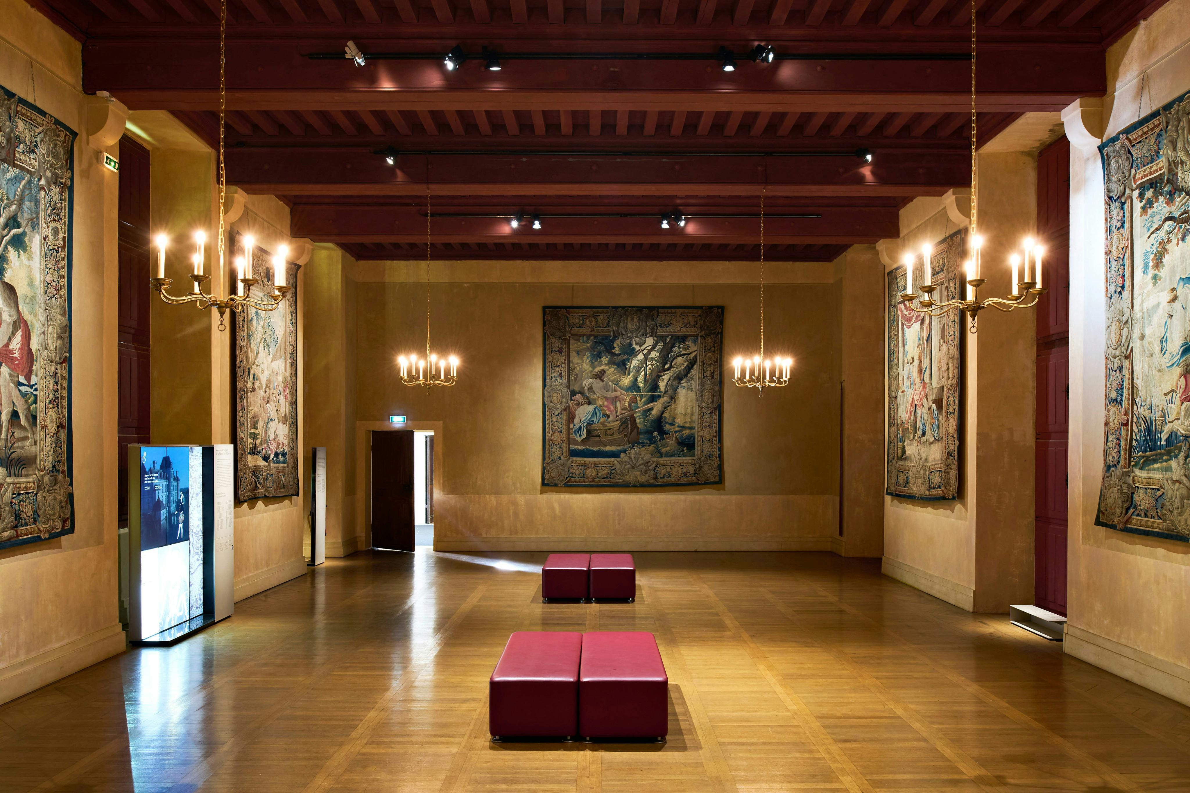 房间宽敞，配有木地板、红色长凳、吊灯和墙上的装饰挂毯。