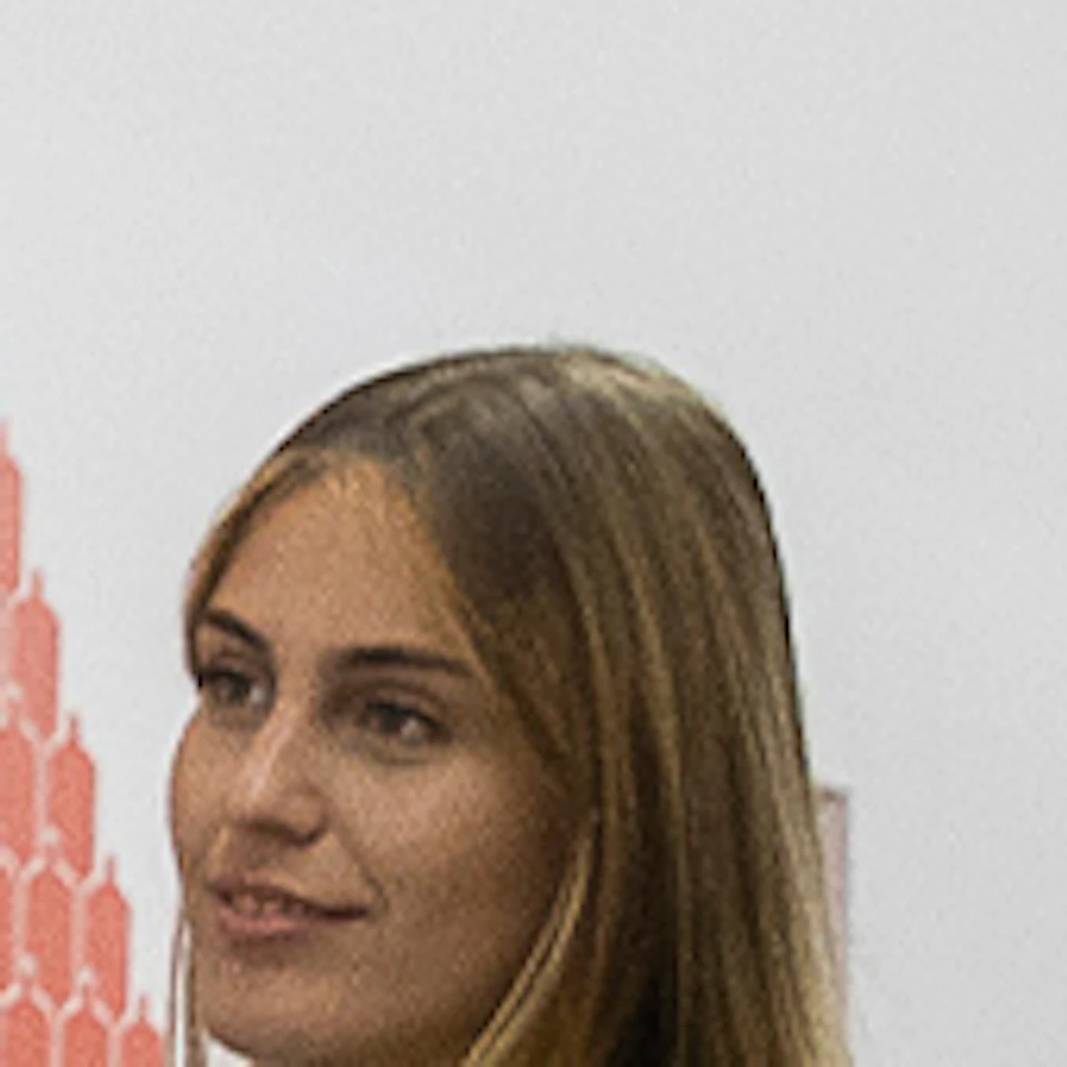 A woman gestures while speaking to a group of three women and one man, with red text and graphics on the white wall behind them.