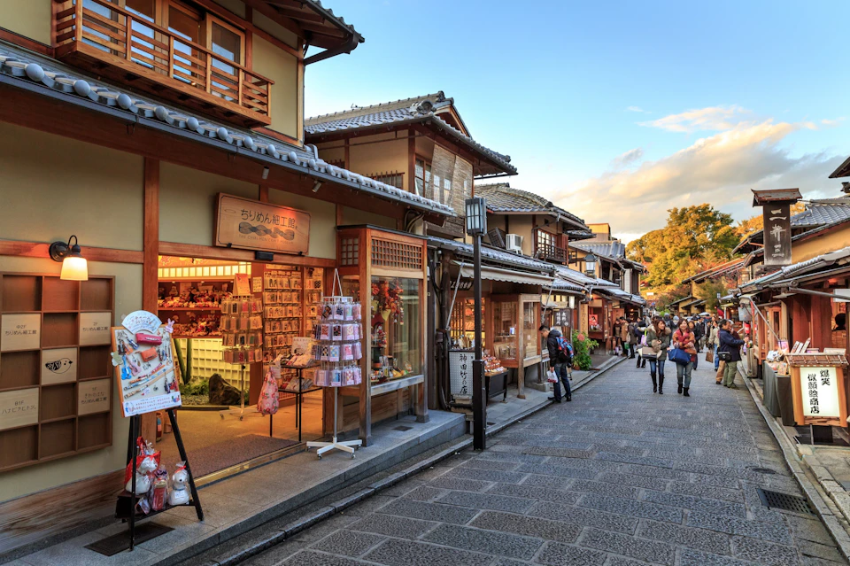 Pedestrian street with traditional Japanese shops, people walking, and a clear evening sky.