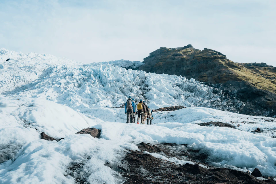 A group of people walking on a snowy glacier with a rocky mountain in the background under a clear sky.