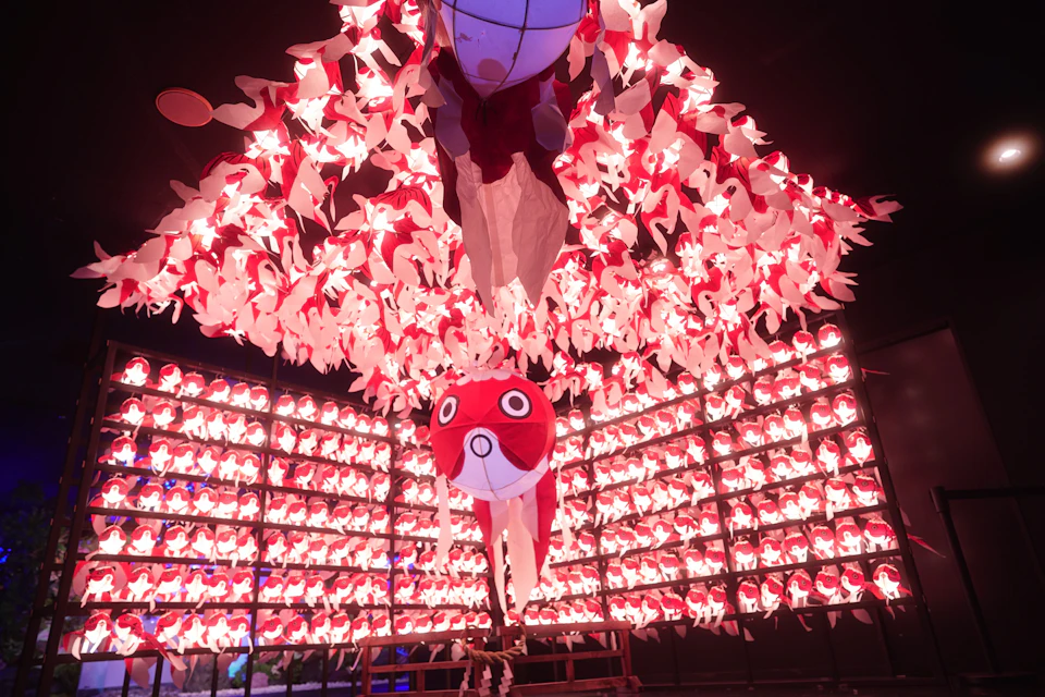 A display of illuminated red and white paper fish decorations in a dark room, arranged in a cascading pattern.