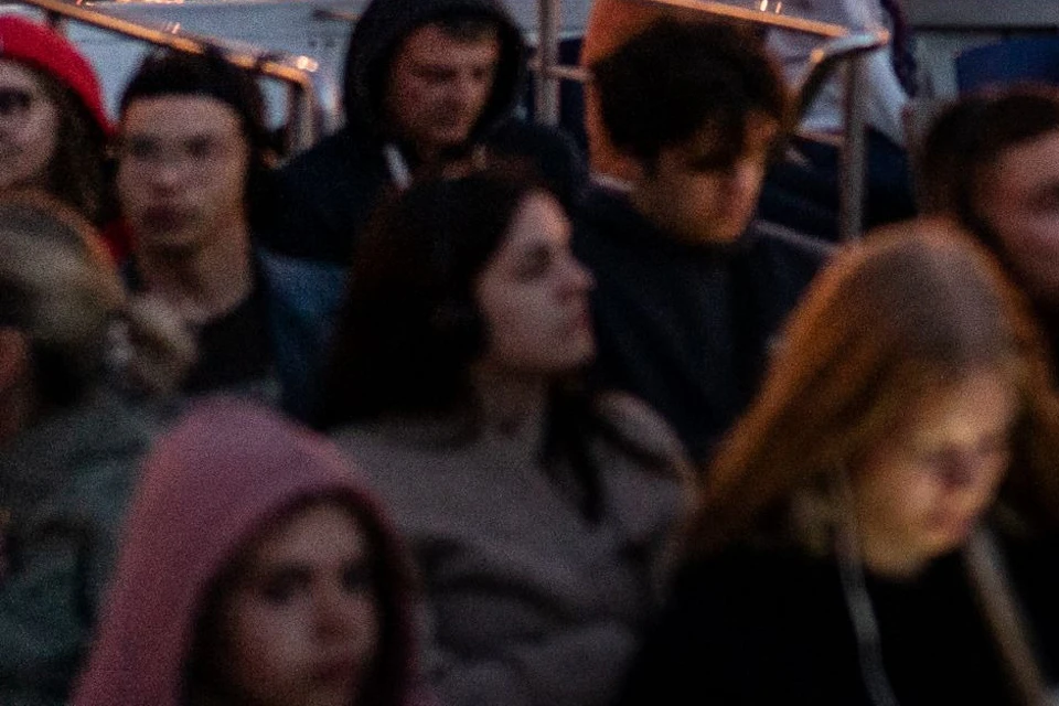 A group of people seated on a boat at dusk with a lit bridge, a hill, and a statue in the background.