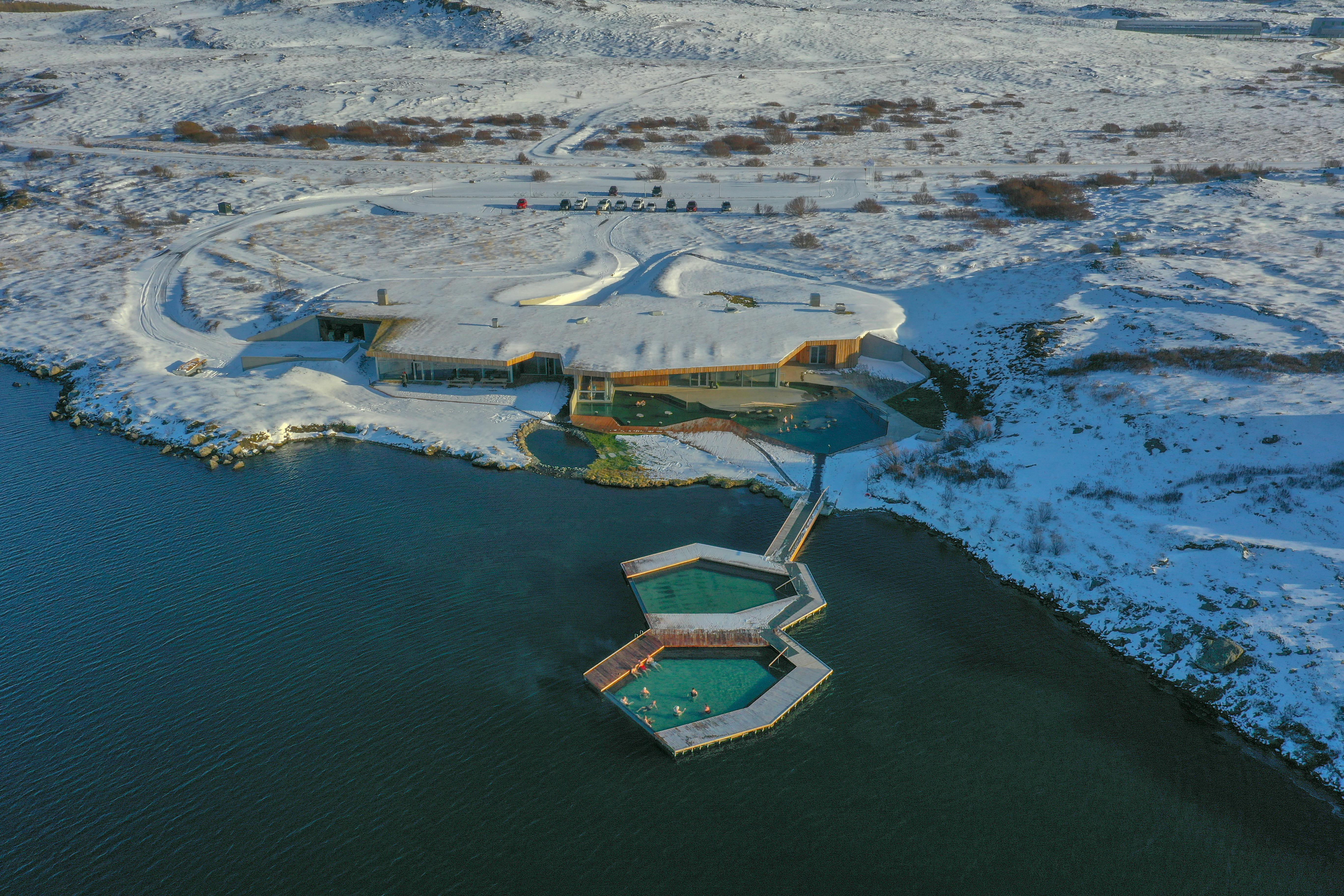 地热池建筑群的鸟瞰图，现代建筑被雪包围，毗邻湖泊。